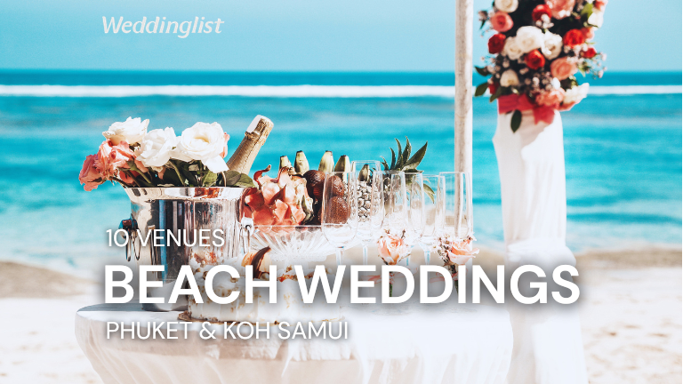 A long reception table beautifully set up on the beach for a wedding, decorated with white and peach flower centerpieces, white chairs, and elegant curtains, representing top wedding hotels in Phuket and Koh Samui.